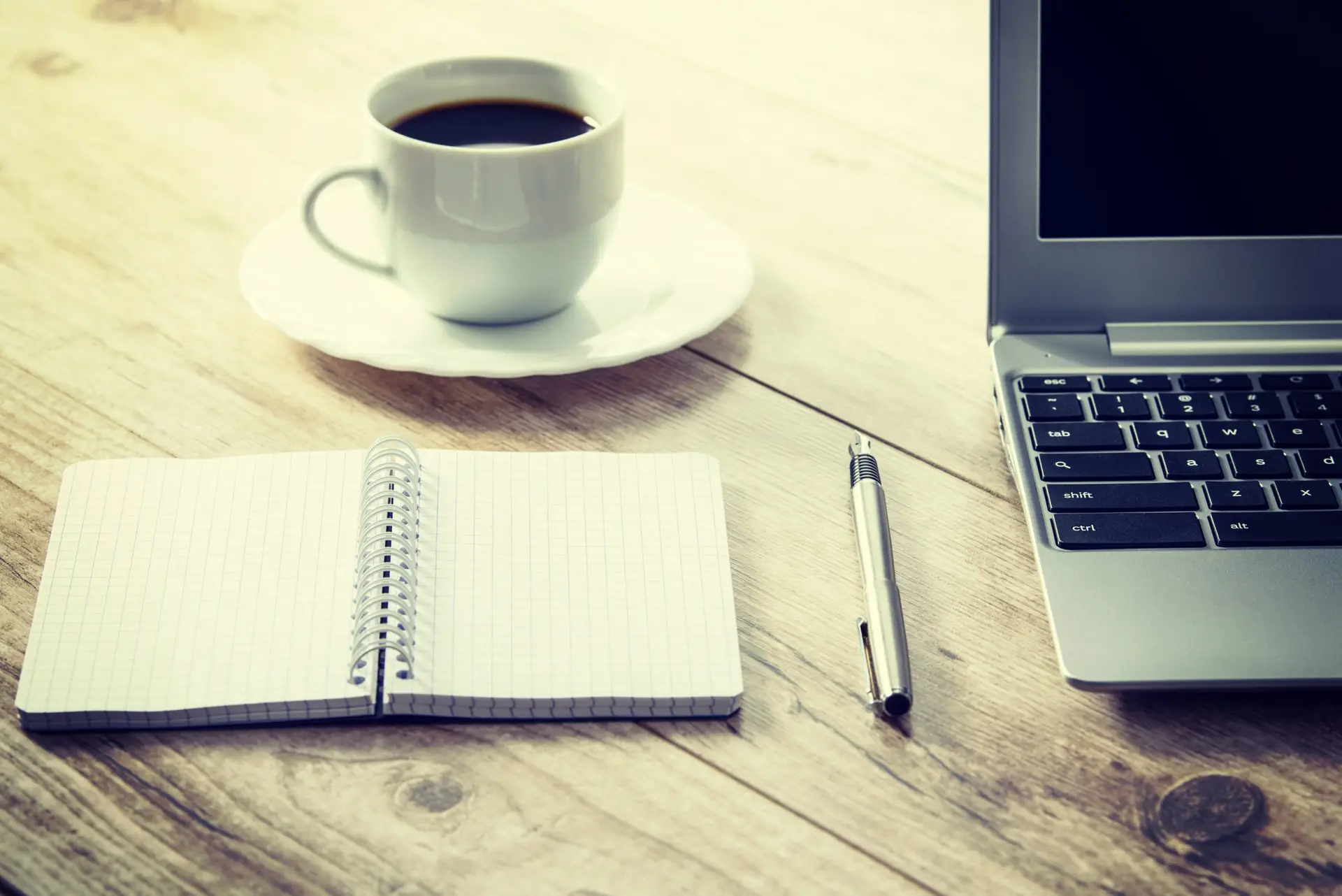 Laptop, notitieblok en kop koffie op de werkplek van de redactie van Kidsphase voor contact en samenwerking.